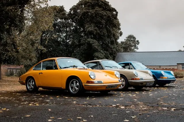 3 Anciennes Porsche de couleur différentes garées sur un Parking extérieur