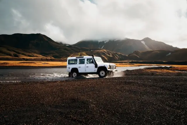 Ancien Land Rover Defender blanc traversant un lac en pleine nature offroad