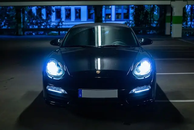 Porsche Boxster noire phares allumés dans un parking
