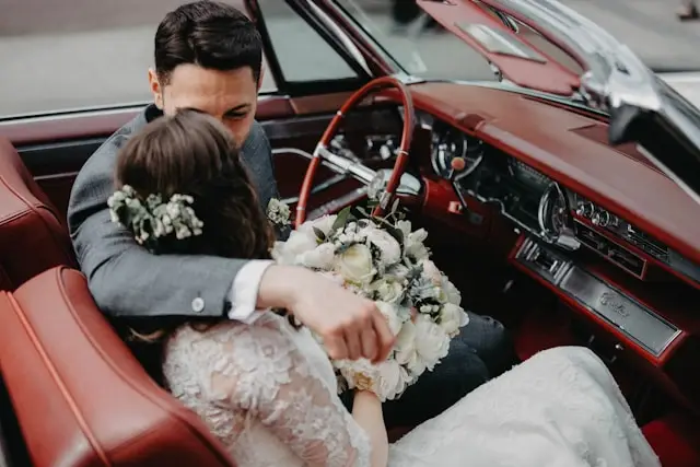 Mariés dans une voiture américaine avec un bouquet de fleurs