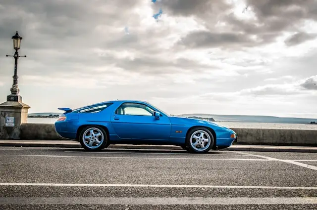 Porsche 928 coupé bleue de côté garée a coté de la mer